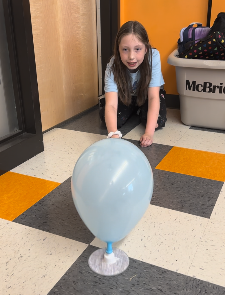 Student watches as her balloon powered hovercraft slides along the floor