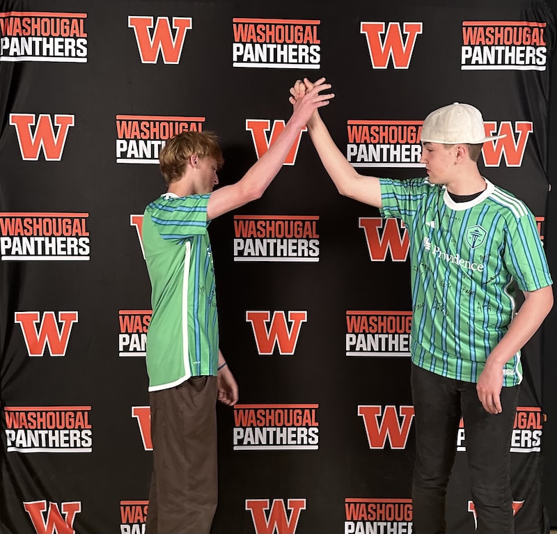 Two WHS students high-five in front of the WHS panthers background, wearing MLS soccer Seattle Sounder shirts