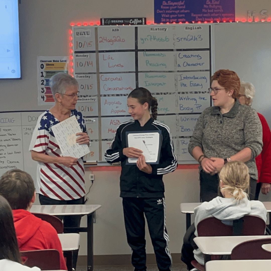 Student receiving award from VFW Auxiliary with teacher watching